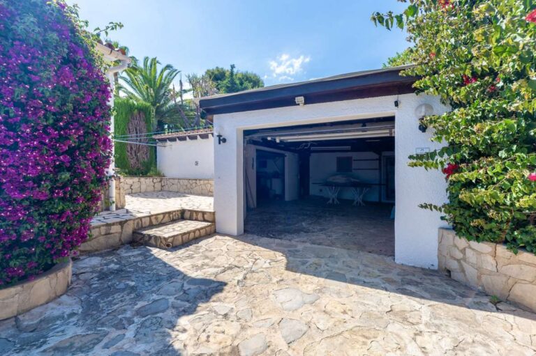 Garage and driveway at a renovated single-level villa in Moraira with stone paving, white exterior walls, flowering bougainvillea and private parking