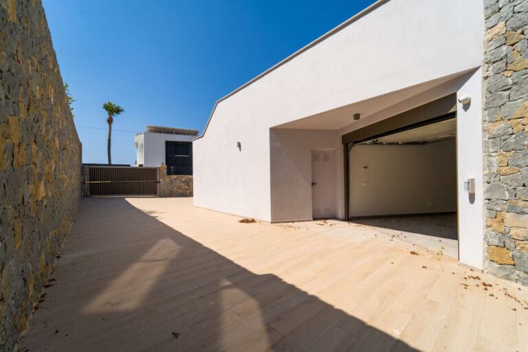 Garageneinfahrt einer neu gebauten Luxusvilla in der Nähe des Yachthafens Puerto Blanco in Calpe mit Steinmauer, modernem Äußeren und gepflasterter Auffahrt