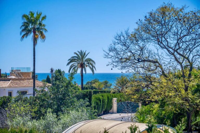 Garden and sea views from a Mediterranean villa in Benissa Costa with palm trees, mature planting and the coastline in the distance
