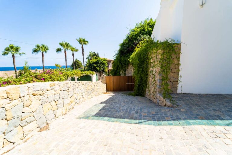 Garden entrance at a luxury villa in Calpe with stone walls, Mediterranean planting, palm trees and sea views in the distance