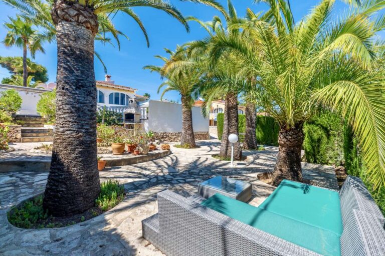 Garden lounge area at a renovated single-level villa in Moraira with outdoor seating, palm trees, stone terrace and Mediterranean planting