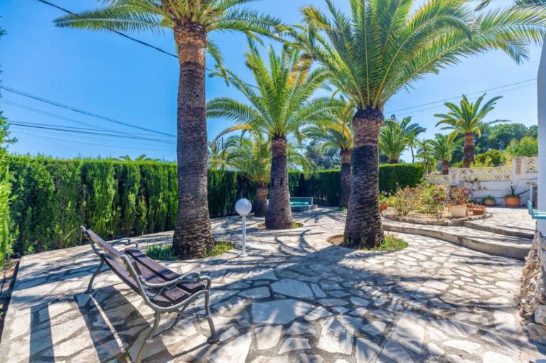 Garden seating area at a renovated single-level villa in Moraira with palm trees, stone paving, sun loungers and Mediterranean planting