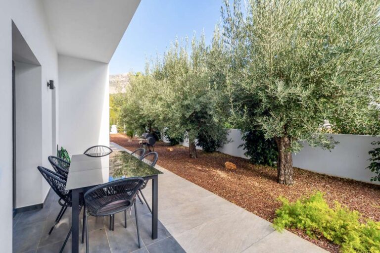 Garden seating area at a single-level modern villa in Santa Clara, Altea with olive trees, tiled walkway, outdoor dining table and private garden