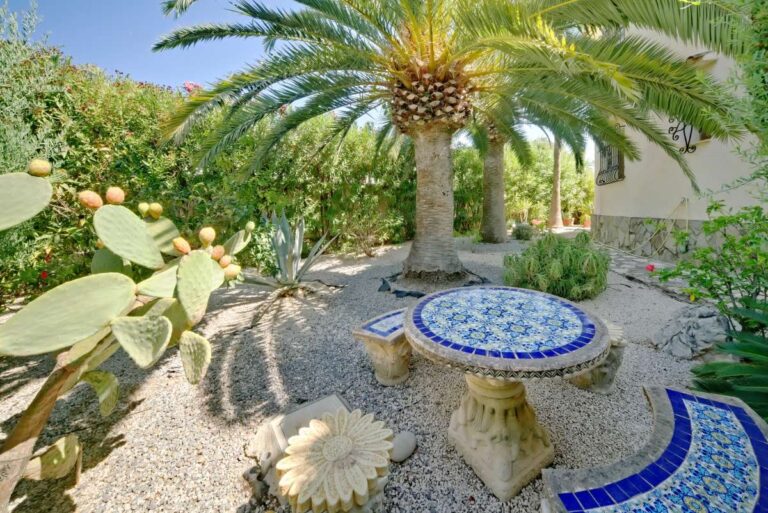 Garden seating area with palm tree, tiled table and Mediterranean planting at a villa near Puerto Blanco in Calpe.