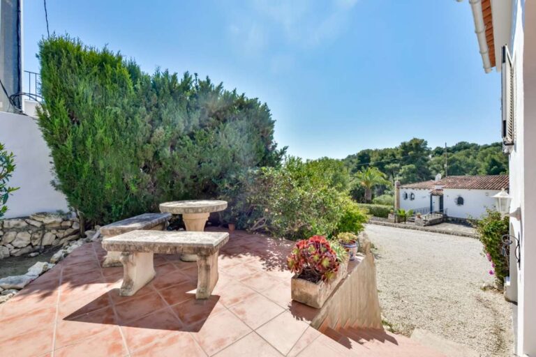 Garden terrace at a charming Benissa Coast villa with stone table, Mediterranean planting, driveway access and surrounding greenery