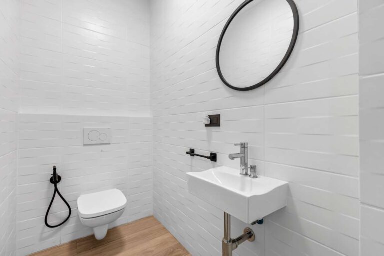 Guest bathroom inside a single-level modern villa in Santa Clara, Altea with wall-mounted toilet, compact sink, round mirror and white tiled finish