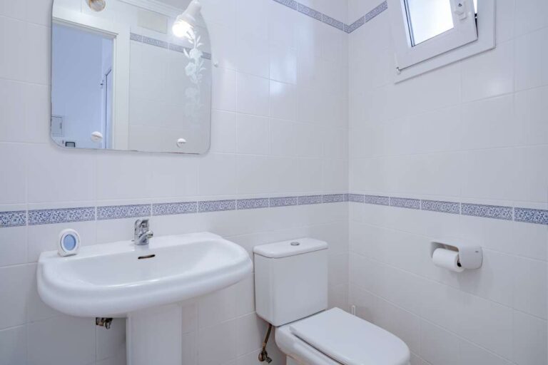 Guest toilet inside a duplex apartment near Les Platgetes Beach in Moraira with pedestal sink, toilet, mirror and white tiled finish