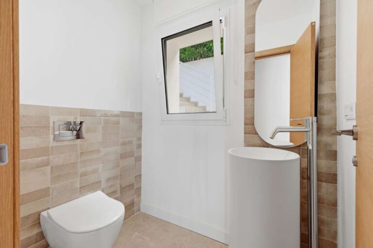 Guest toilet inside a modern villa in Altea Hills with wall-mounted toilet, window, neutral tiled finish and bright interior