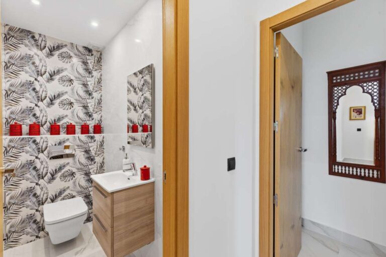 Guest toilet inside a premium coastal villa on the Benissa Costa with patterned wall finish, small vanity unit and hallway access