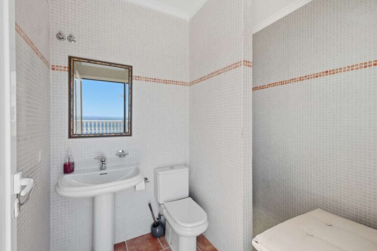 Guest toilet inside an elegant Mediterranean villa in Altea Hills with basin, toilet, mirror and simple bright tiled finish