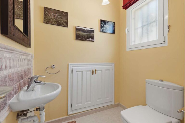 Guest toilet inside an elegant Mediterranean villa in Altea Hills with yellow walls, small basin, toilet and bright window