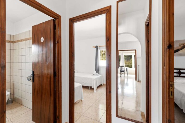 Hallway inside a charming Benissa Coast villa with access to bedrooms and bathroom, wooden doors, mirror and tiled floor