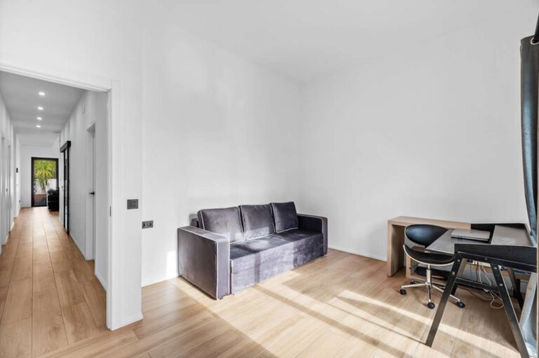 Home office inside a single-level modern villa in Santa Clara, Altea with sofa, desk area, wood flooring, hallway access and bright white interior