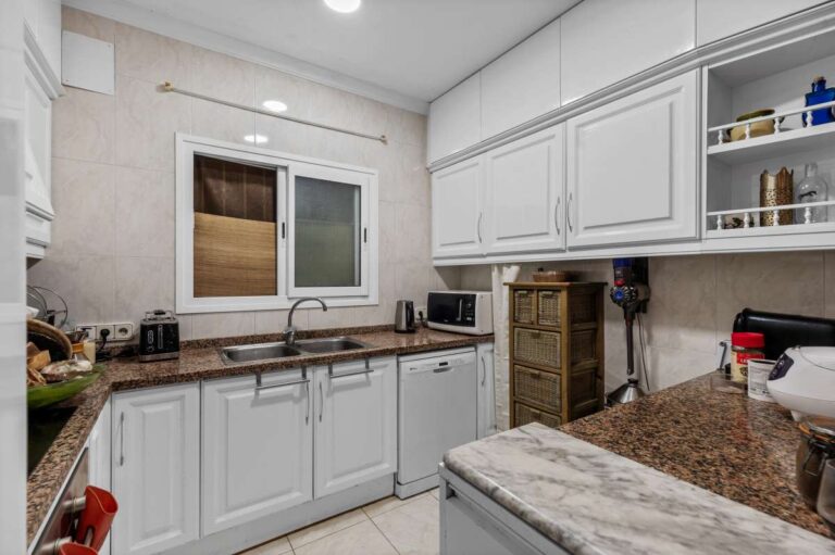 Independent kitchen inside a Benissa sea view villa with white cabinetry, granite worktops, window and built-in storage