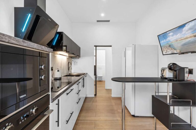 Independent kitchen inside a single-level modern villa in Santa Clara, Altea with black and white cabinetry, integrated appliances and wood flooring