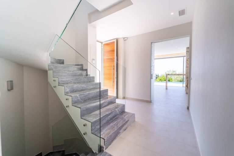 Innentreppe in einer neu gebauten Luxusvilla in der Nähe des Yachthafens Puerto Blanco in Calpe mit Glasgeländer, Stufen in Marmoroptik und hellem, modernem Flur