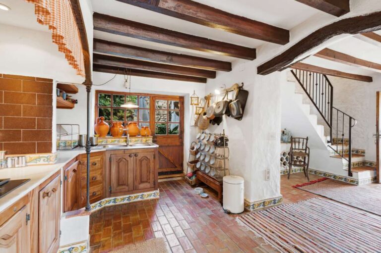 Kitchen and staircase area inside a traditional Spanish finca near Moraira with wooden cabinetry, beamed ceiling, tiled floor and rustic Mediterranean details