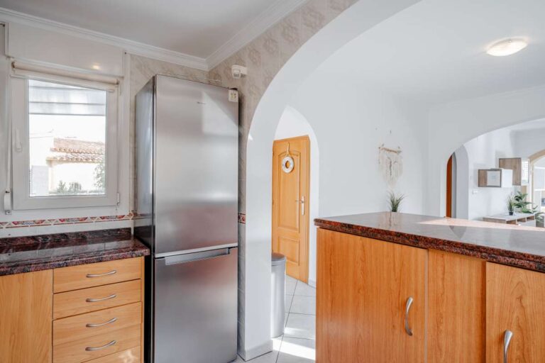 Kitchen area in a Calpe villa with wooden cabinets, fridge freezer and arched opening to the living space