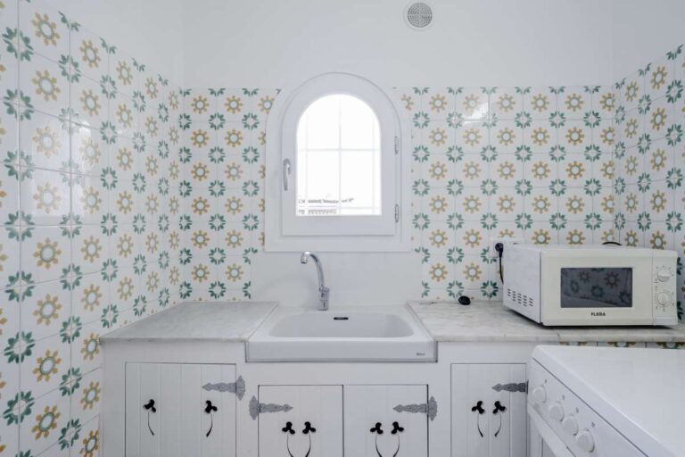 Kitchen detail with patterned tiled walls, white cabinets and arched window inside a Mediterranean villa in Maryvilla, Calpe.