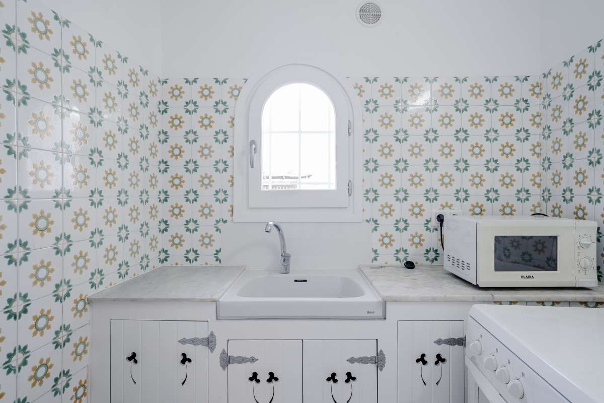 Kitchen detail with patterned tiled walls, white cabinets and arched window inside a Mediterranean villa in Maryvilla, Calpe.