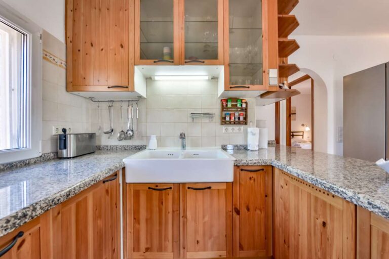 Kitchen inside a charming Benissa Coast villa with wooden cabinetry, granite worktops, sink, window and integrated storage