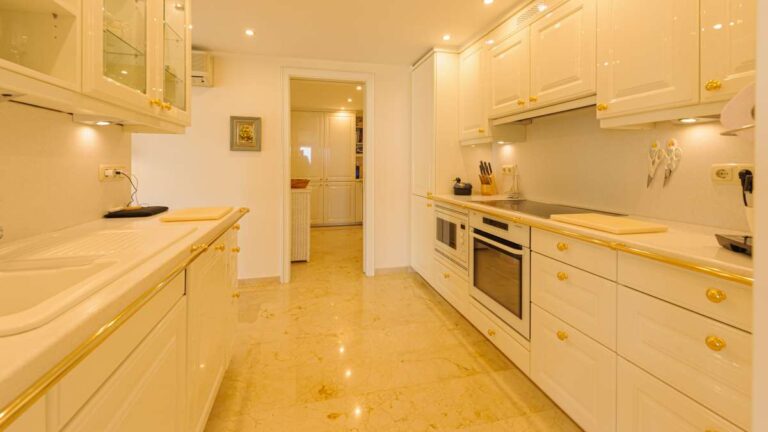 Kitchen inside a luxury apartment in Sierra de Altea with white cabinets, generous worktops, built-in appliances and marble flooring
