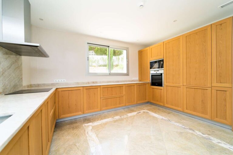 Kitchen inside a luxury villa in Calpe with wood cabinetry, built-in appliances, marble flooring and natural light