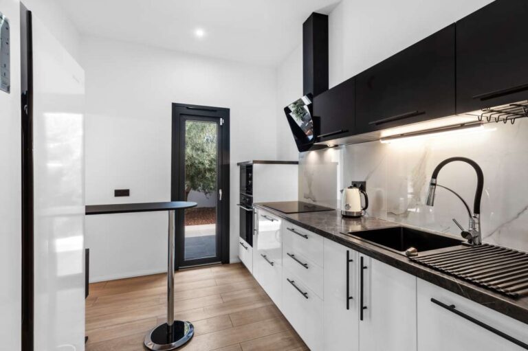 Kitchen inside a single-level modern villa in Santa Clara, Altea with high-end appliances, black sink, white cabinetry and exterior access