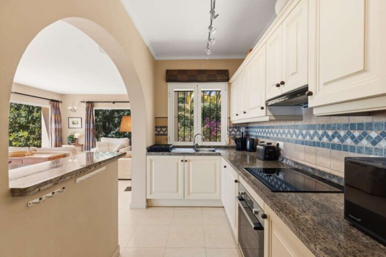 Kitchen inside an elegant Mediterranean villa in Altea Hills with arched opening, cream cabinetry, granite worktops and garden views