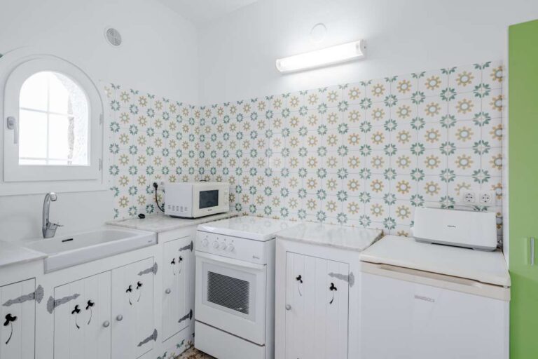 Kitchen with white cabinetry, arched window and patterned tiles inside an independent apartment at a Mediterranean villa in Maryvilla, Calpe.