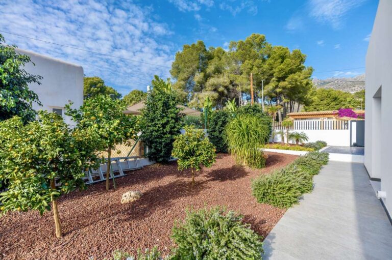 Landscaped garden at a single-level modern villa in Santa Clara, Altea with mature planting, tiled walkway, private pool area and mountain backdrop