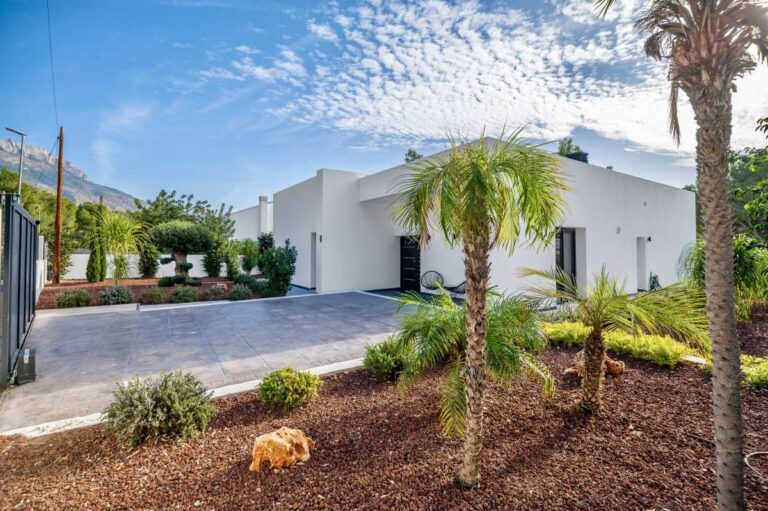 Landscaped garden at a single-level modern villa in Santa Clara, Altea with palm trees, white exterior, private driveway and mountain backdrop