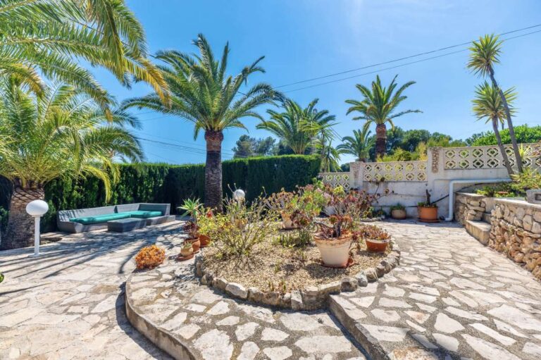 Landscaped garden terrace at a renovated single-level villa in Moraira with palm trees, stone paving, raised planting beds and outdoor seating