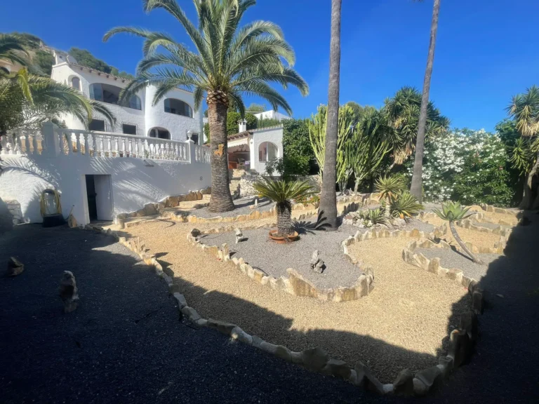 Landscaped Mediterranean garden with palm trees, gravel areas, and stone borders at a villa in Calpe.