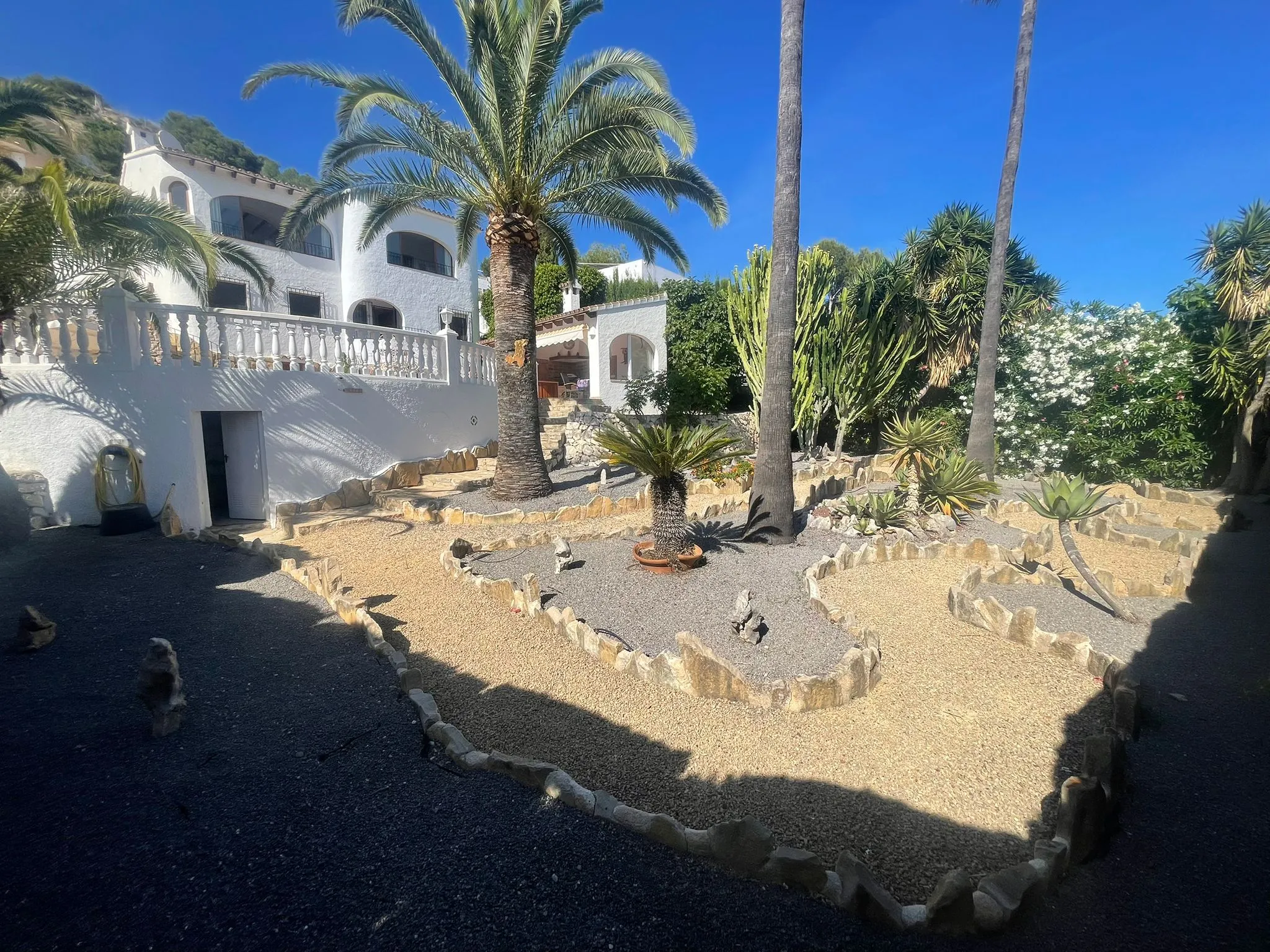 Landscaped Mediterranean garden with palm trees, gravel areas, and stone borders at a villa in Calpe.