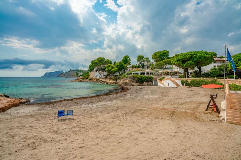 Les Platgetes Beach in Moraira with sandy shoreline, Mediterranean Sea, coastal walkway, trees and beachside surroundings