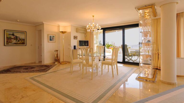 Living and dining area inside a luxury apartment in Sierra de Altea with marble flooring, dining table, chandelier lighting and terrace access