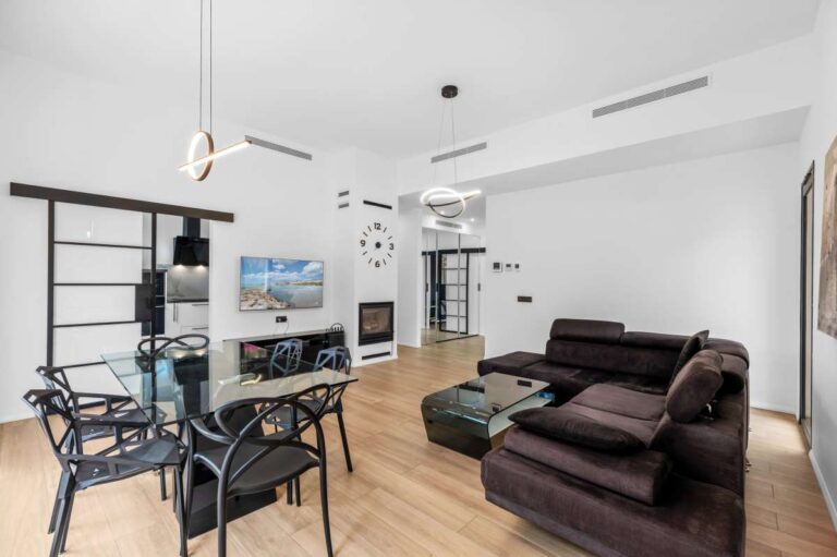 Living and dining area inside a single-level modern villa in Santa Clara, Altea with wood-burning fireplace, sofa seating, dining table and modern lighting