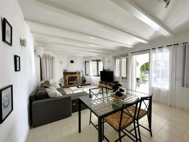 Living and dining area inside a single-level villa near El Portet Beach in Moraira with fireplace, sofa seating, dining table and natural light