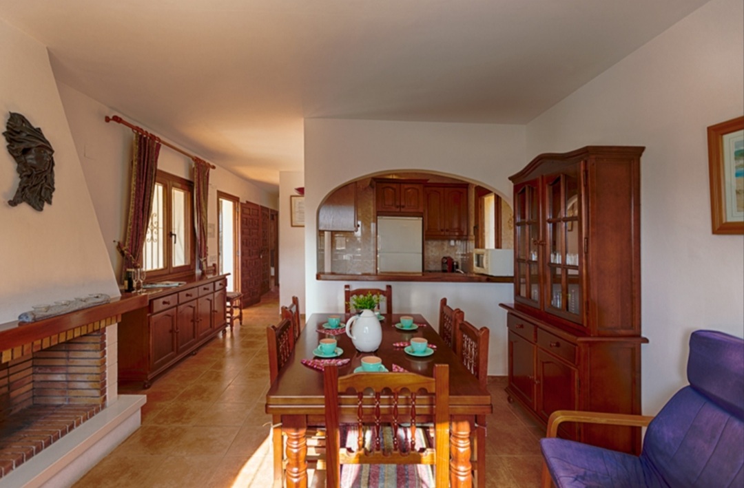 Living and dining area with open kitchen, fireplace and traditional wooden furniture inside a Mediterranean villa in Calpe.