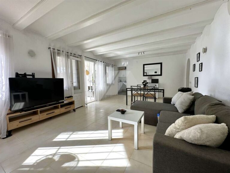 Living and dining room inside a single-level villa near El Portet Beach in Moraira with sofa seating, TV area, white beamed ceiling and natural light
