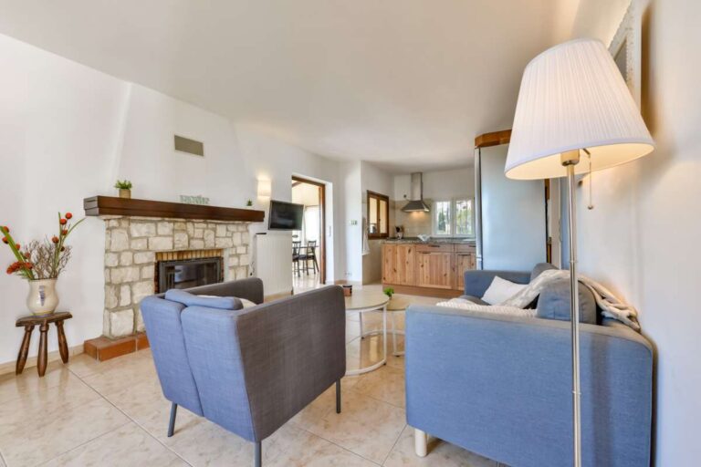 Living area inside a charming Benissa Coast villa with sofa seating, stone fireplace, open-plan kitchen and bright Mediterranean interior