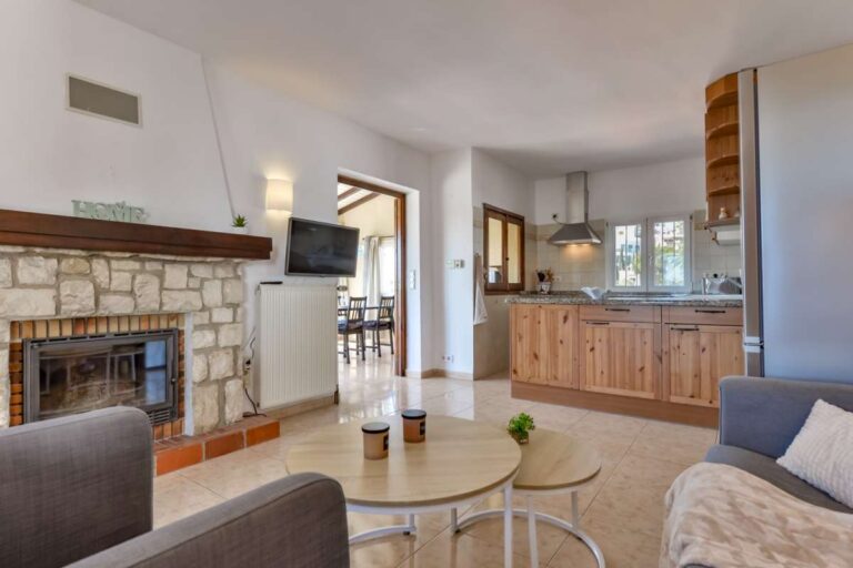 Living area inside a charming Benissa Coast villa with stone fireplace, open-plan kitchen, sofa seating and bright Mediterranean interior