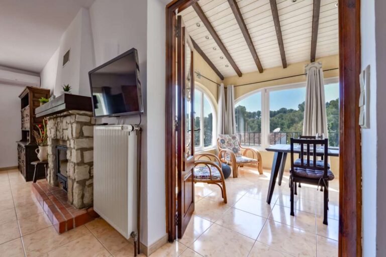 Living area inside a charming Benissa Coast villa with stone fireplace, TV area and access to a bright dining room with garden views