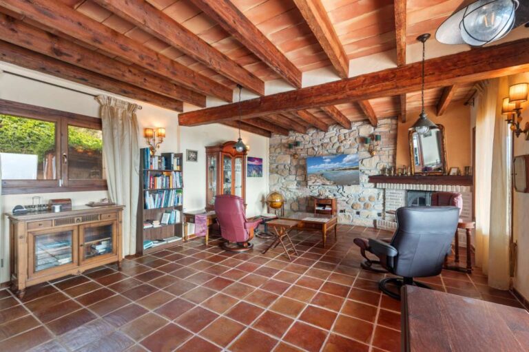 Living area inside a finca-style villa in Benissa Costa with wooden beams, terracotta tiled floor, stone wall, fireplace and sea views