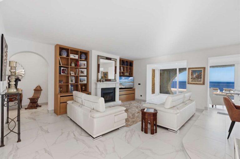 Living room inside a premium coastal villa on the Benissa Costa with white sofa seating, built-in shelving and sea views through large windows
