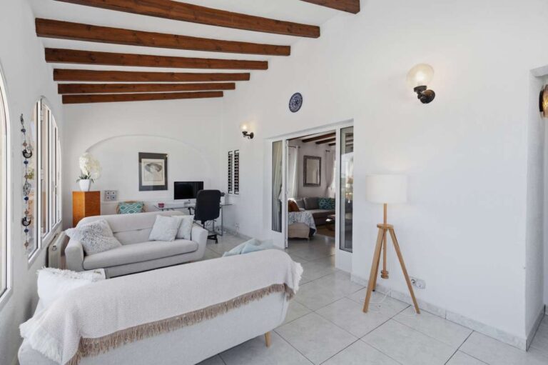 Living room inside a renovated single-level villa in Moraira with beamed ceiling, fireplace, sofa seating and bright Mediterranean interior