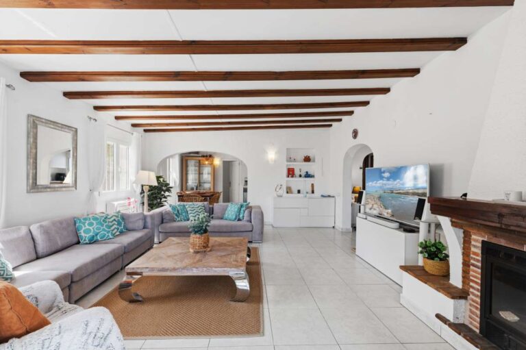 Living room inside a renovated single-level villa in Moraira with fireplace, exposed beams, sofa seating and TV area