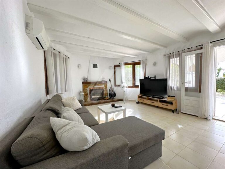 Living room inside a single-level villa near El Portet Beach in Moraira with sofa seating, fireplace, white beamed ceiling and garden access
