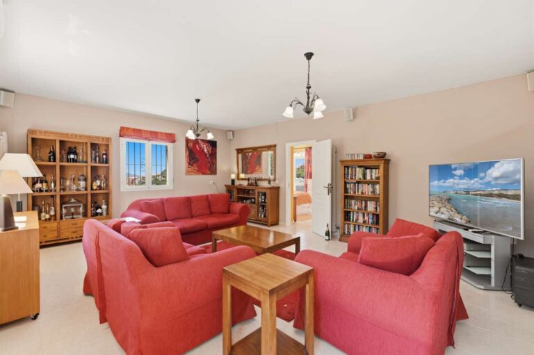 Living room inside an Altea Hills villa with red sofa seating, TV area, bookshelves and direct terrace access